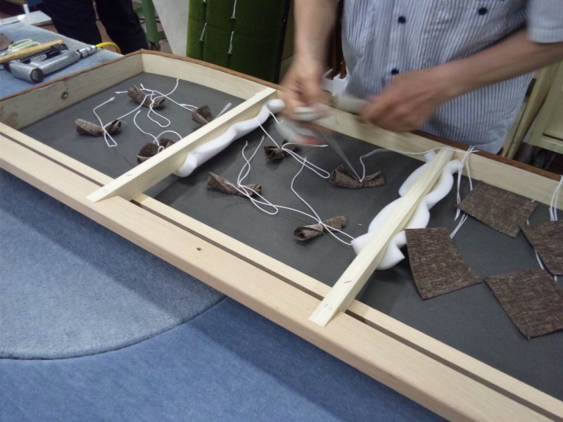 Kチェア2シーター本革の座面のボタンを手作業で取り付けする風景